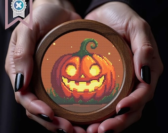 Può includere: Un sottobicchiere rotondo in legno con un disegno a punto croce di una zucca sorridente su sfondo arancione. Il sottobicchiere è tenuto in due mani. Un'etichetta di download PDF si trova nell'angolo in alto a sinistra.