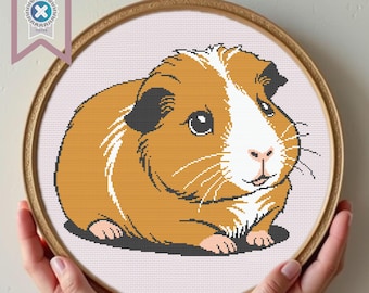 May include: A cross-stitch pattern of a brown and white guinea pig with black eyes and a pink nose. The guinea pig is lying on its side with its head turned to the right.