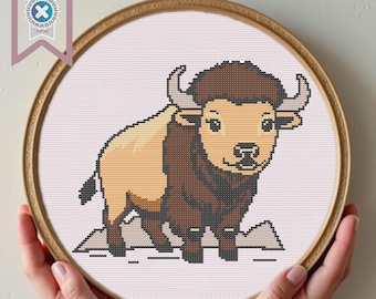 May include: A cross-stitch pattern of a brown and tan bison with a white background. The bison is standing on a small patch of brown ground.
