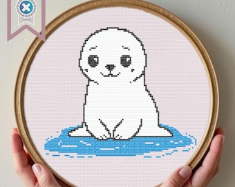 May include: A white seal with black eyes and a black nose sits on a blue ice floe. The seal is sitting up with its paws tucked under its chin. The ice floe is surrounded by blue water.