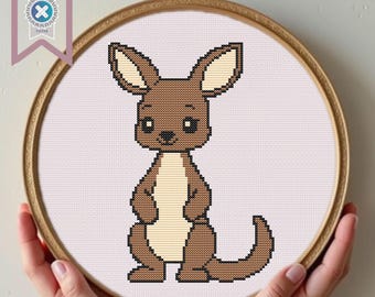 Può includere: Un ricamo a punto croce di un canguro dei cartoni animati in un telaio di legno. Il canguro è marrone con la pancia color crema e grandi orecchie. Il telaio è tenuto da mani. Uno striscione in alto a sinistra recita "PDF Download Tested".