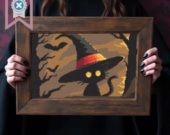 Può includere: Opera d'arte a punto croce in una cornice di legno raffigurante un gatto nero con un cappello da strega e occhi gialli. Lo sfondo presenta pipistrelli e alberi nei toni del marrone e dell'arancione, a tema Halloween.