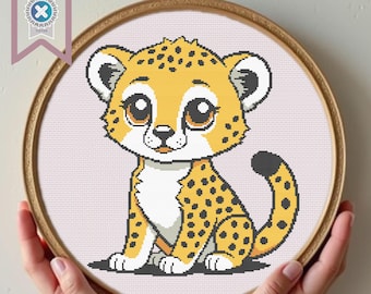 May include: Cross-stitch embroidery of a cartoon cheetah cub in a wooden hoop. The cheetah has yellow fur with black spots, large brown eyes, and a white belly. The hoop is held by hands, and a PDF download tag is visible.
