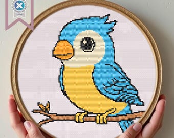 Può includere: Uno schema di punto croce di un uccello blu e giallo appollaiato su un ramo. L'uccello ha occhi grandi e rotondi e un piccolo becco.