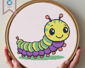 Può includere: Uno schema di punto croce di un bruco dei cartoni animati con una testa gialla, un corpo verde e giallo e gambe viola. Il bruco ha occhi grandi e un viso sorridente.