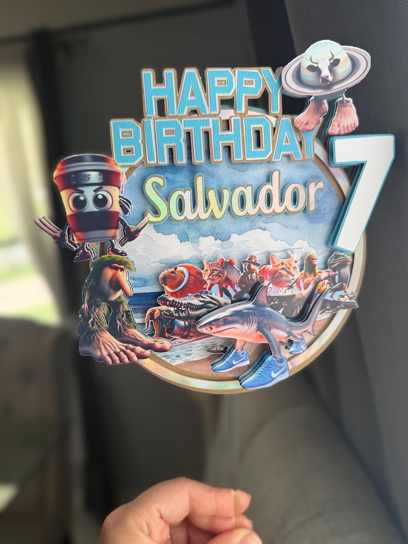 Może przedstawiać: Kolorowa dekoracja na tort urodzinowy z napisem "HAPPY BIRTHDAY Salvador" w kolorze niebieskim i białym. Wyświetlana jest liczba 7. Dekoracja zawiera postacie z kresk&oacute;wek, w tym rekina w trampkach, filiżankę kawy i kosmitę.