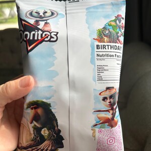 May include: A white bag of Doritos crisps with a birthday theme. The bag features a cartoon cow wearing a hat and holding a pineapple. The bag also has a nutrition facts label and a QR code. The text on the bag reads "Birthday Nutrition Facts" and "@teenytiny_favors".