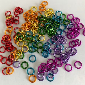 May include: A large assortment of colorful metal jump rings in rainbow colors. The rings are small and perfect for jewelry making or crafting.