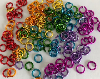 May include: A large assortment of colorful metal jump rings in rainbow colors. The rings are small and perfect for jewelry making or crafting.