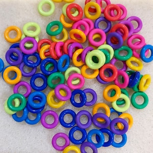 May include: A collection of colorful plastic rings in various shades, including red, orange, yellow, green, blue, and purple. These small, round objects are scattered across a light-colored surface, creating a vibrant and playful display. Ideal for crafting or educational purposes.
