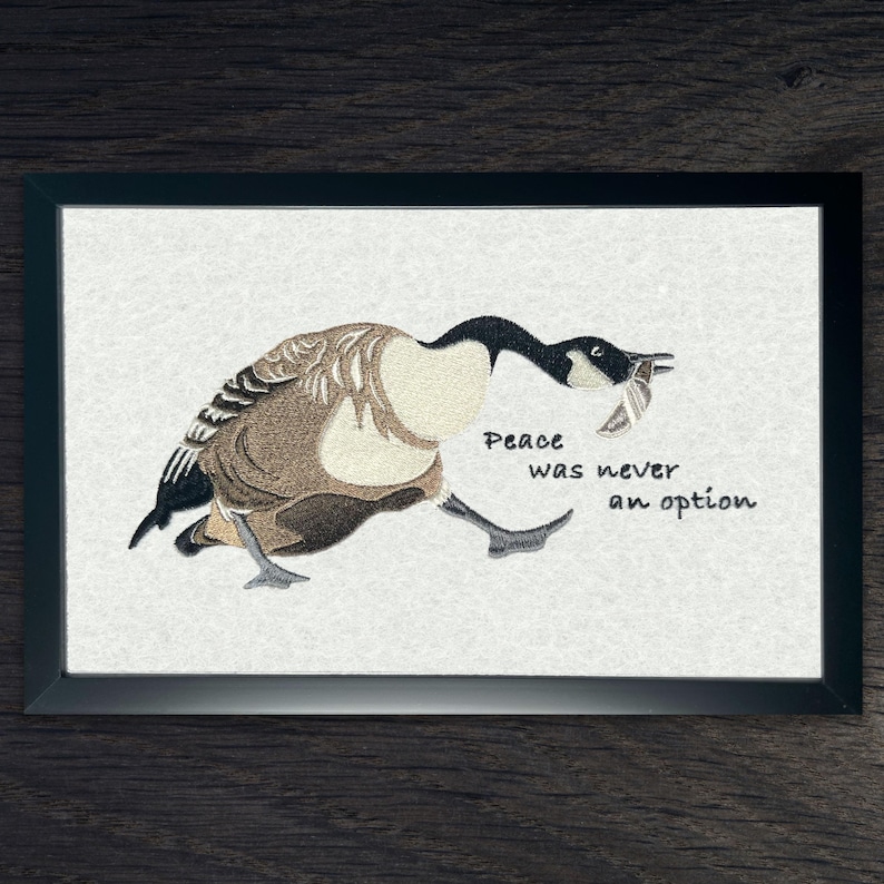 Peace was never an option. Murder goose embroidery in black frame – Satirical goose meme artwork.