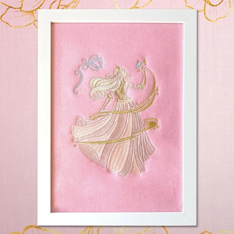 Pink embroidery detail of the princess in a gold-pink dress surrounded by magical gold particles.