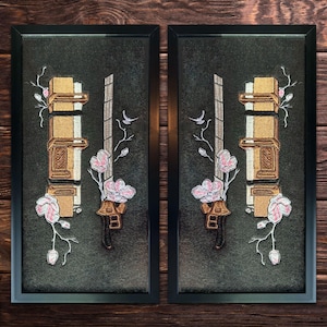 May include: Two framed black and white embroidered wall art pieces with a dark green background. Each piece features a gold and white design with a sword and flowers.