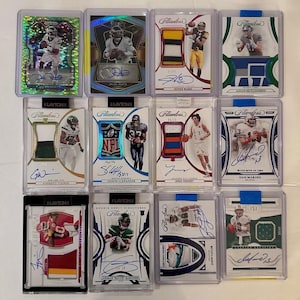 May include: A collection of football trading cards in protective cases. The cards feature player images, autographs, and jersey patches. The cards are from the Flawless and Layton brands, with various designs and colors.