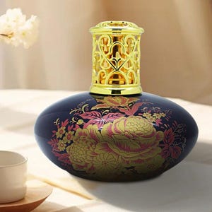 May include: A dark blue ceramic aromatherapy lamp with a gold filigree top and floral design. The lamp features a gold and pink floral pattern on the body. The top is a decorative gold metal with an openwork design.