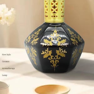 May include: A black ceramic aromatherapy lamp with gold floral designs. The lamp has a gold-colored top and is labeled "New Style", "Ceramic", "Aromatherapy", and "Lamp". The lamp is an elegant home decor item.