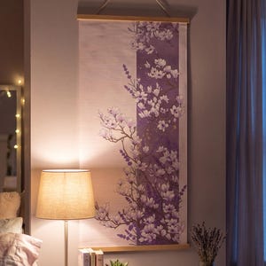 May include: A vertical wall hanging featuring a light pink background with a central purple panel decorated with white and purple floral illustrations of magnolia blossoms and lavender sprigs, suspended from a light wood frame with a white cord.