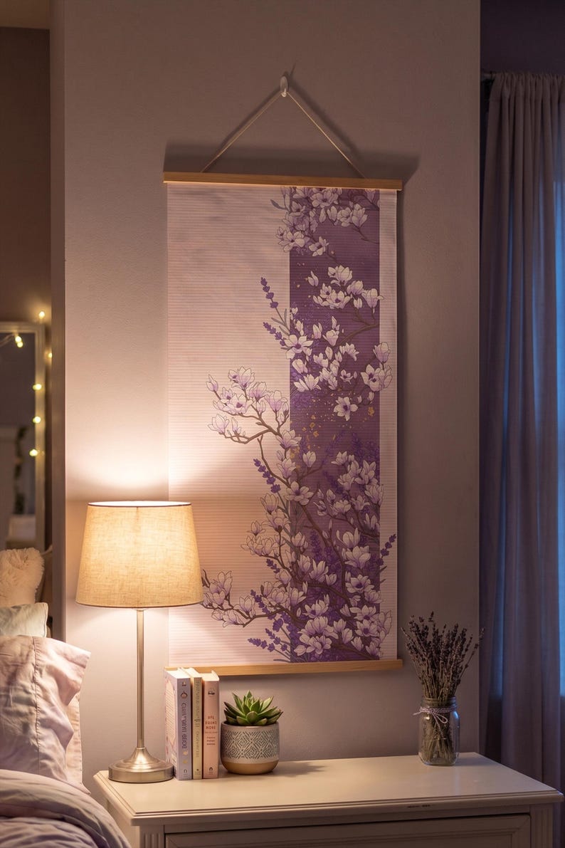 May include: A vertical wall hanging featuring a light pink background with a central purple panel decorated with white and purple floral illustrations of magnolia blossoms and lavender sprigs, suspended from a light wood frame with a white cord.