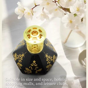 May include: Black hexagonal fragrance diffuser with gold filigree design and a gold top. The diffuser is decorated with gold floral patterns. White flowers in a glass vase are in the background. The text on the image says: Suitable in size and space, hotels, shopping malls, and leisure clubs, and home.