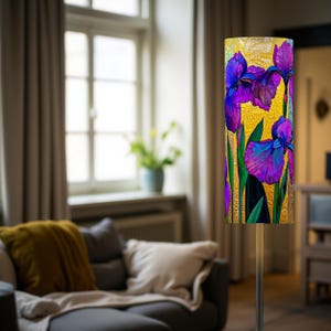 May include: A floor lamp with a cylindrical shade featuring a vibrant floral design. The artwork showcases purple irises with green stems against a golden yellow background. The lamp's metal stand is silver.