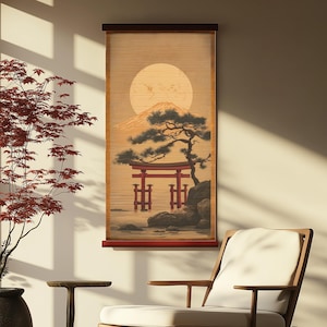 May include: A Japanese-themed wall hanging featuring a scenic landscape. The artwork depicts a large, full moon, a mountain, a traditional red torii gate, and a stylized tree. The background is a light tan color, and the frame is dark brown.