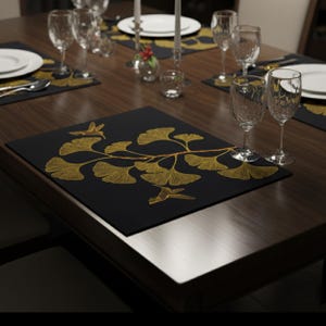 May include: A dining table set with black placemats, each adorned with a gold ginkgo leaf and hummingbird motif. The table is set with white plates, crystal wine glasses, and cutlery, creating a refined and stylish dining experience.