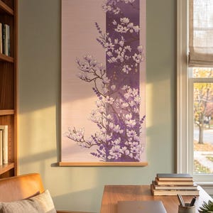 May include: A vertical wall hanging featuring a floral illustration of white magnolia blossoms and purple lavender sprigs. The artwork is printed on a light pink background with a dark purple vertical stripe, suspended by wooden rods at the top and bottom.