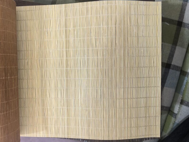 May include: A light beige bamboo blind featuring thin, vertical slats held together by fine, evenly spaced horizontal threads. The material has a natural, fibrous texture with subtle variations in color, showcasing a clean, linear pattern.