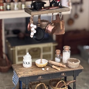 Op de afbeelding: Miniatuurkeuken met een houten tafel en hangende potten en pannen. De tafel heeft een bloempot, kom, deegroller en manden. Een klein zwart fornuis staat op de achtergrond. Een charmante, gedetailleerde weergave van een keuken.