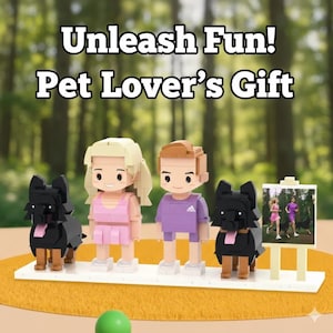 May include: A pet-themed gift set featuring block figures of two people, two black dogs, and a small framed picture. The figures stand on a white base with a green ball in the foreground. The text "Unleash Fun! Pet Lover's Gift" is at the top.