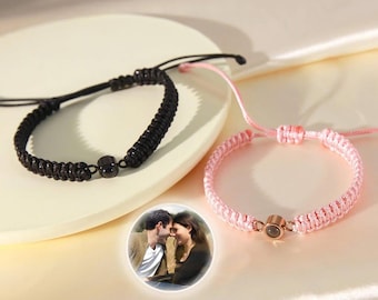 May include: Two matching friendship bracelets with a small round charm that reveals a photo when held up to the light. The bracelets are black and pink with a black and gold charm.