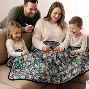 May include: A black and white floral patterned blanket with select flowers colored in shades of teal, yellow, and red. The blanket features a solid black border and is being colored with markers by individuals using various colored ink pens.