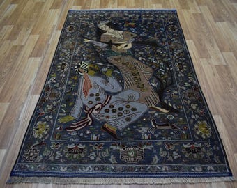 Puede incluir: Una alfombra azul con un patrón floral y dos figuras en el centro. Las figuras visten ropa tradicional y están rodeadas de flores y enredaderas. La alfombra tiene un borde de flecos.