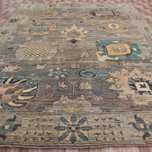 May include: A large, rectangular area rug with an intricate floral pattern. The rug features a muted color palette of blues, tans, and greens. The design includes stylized flowers and geometric shapes, creating a traditional aesthetic.