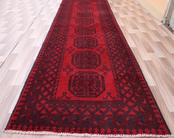 May include: A red and black runner rug with a traditional geometric pattern. The rug has a fringe border and is made of wool.