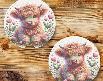 May include: Two round white ceramic coasters with a colorful illustration of a Highland cow with pink hearts and flowers.