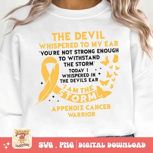 Puede incluir: Sudadera blanca con el texto "THE DEVIL WHISPERED TO MY EAR" y "I AM THE STORM". Presenta una cinta amarilla y gráficos de mariposas, con las palabras "APPENDIX CANCER WARRIOR".