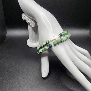 May include: A double-strand bracelet with green and white beads and a white cross charm.