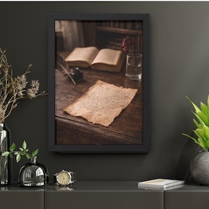 Könnte beinhalten: Gerahmter Druck mit einem Vintage-Stillleben. Das Bild zeigt ein offenes Buch, einen handgeschriebenen Brief, ein Tintenfass mit einer Feder und ein Glas Wasser mit einer getrockneten Rose auf einem Holztisch. Der Rahmen ist schwarz.