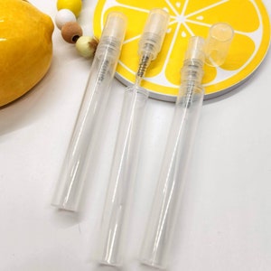 Könnte beinhalten: Drei klare, nachfüllbare Parfümfläschchen aus Glas mit gelben Kappen auf einem gelben Zitronenscheiben-Hintergrund. Die Fläschchen sind leer und bereit, mit Ihrem Lieblingsduft gefüllt zu werden.