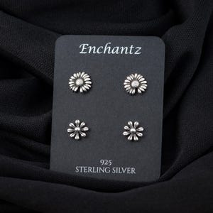 May include: Four silver daisy flower stud earrings on a black card with the text "Enchantz 925 Sterling Silver".