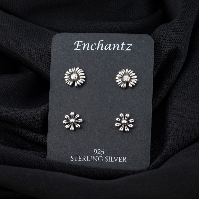 May include: Four silver daisy flower stud earrings on a black card with the text "Enchantz 925 Sterling Silver".