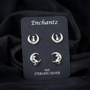 May include: A set of four silver-colored stud earrings on a black card. Each earring features a crescent moon with a cat silhouette. The card is labeled "Enchantz" and "925 STERLING SILVER".