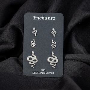 May include: A black card displays six sterling silver snake stud earrings. The card reads "Enchantz" at the top and "925 STERLING SILVER" at the bottom. The earrings are in three different sizes and designs.