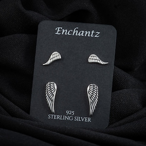 May include: A set of four silver angel wing earrings on a black card with the text "Enchantz 925 Sterling Silver".