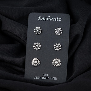 May include: A set of six silver daisy stud earrings on a black card with the text "Enchantz 925 Sterling Silver".