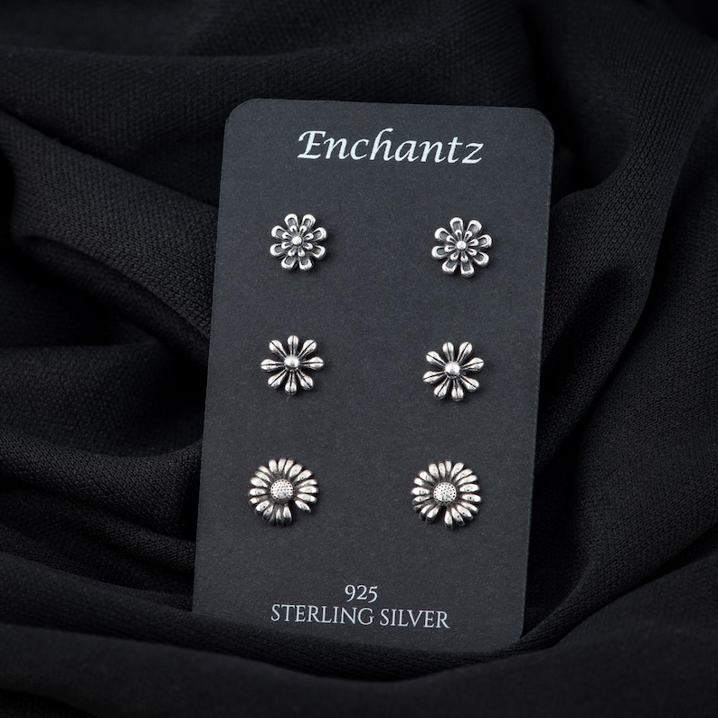 May include: A set of six silver daisy stud earrings on a black card with the text "Enchantz 925 Sterling Silver".