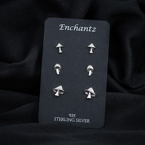 May include: A set of six sterling silver mushroom earrings. The earrings are displayed on a black card with the word "Enchantz" and "925 Sterling Silver" printed on it.
