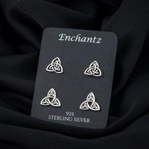 May include: A set of four sterling silver earrings featuring a Celtic knot design. The earrings are displayed on a black card with the brand name "Enchantz" and the text "925 Sterling Silver".