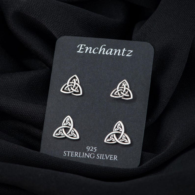 May include: A set of four sterling silver earrings featuring a Celtic knot design. The earrings are displayed on a black card with the brand name "Enchantz" and the text "925 Sterling Silver".